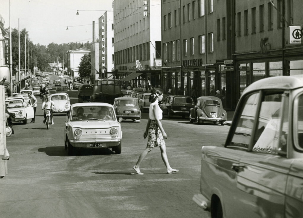 Vanha mustavalkoinen valokuva Riihimäen Hämeenkadulta, jossa nuori nainen ylittää suojatietä.