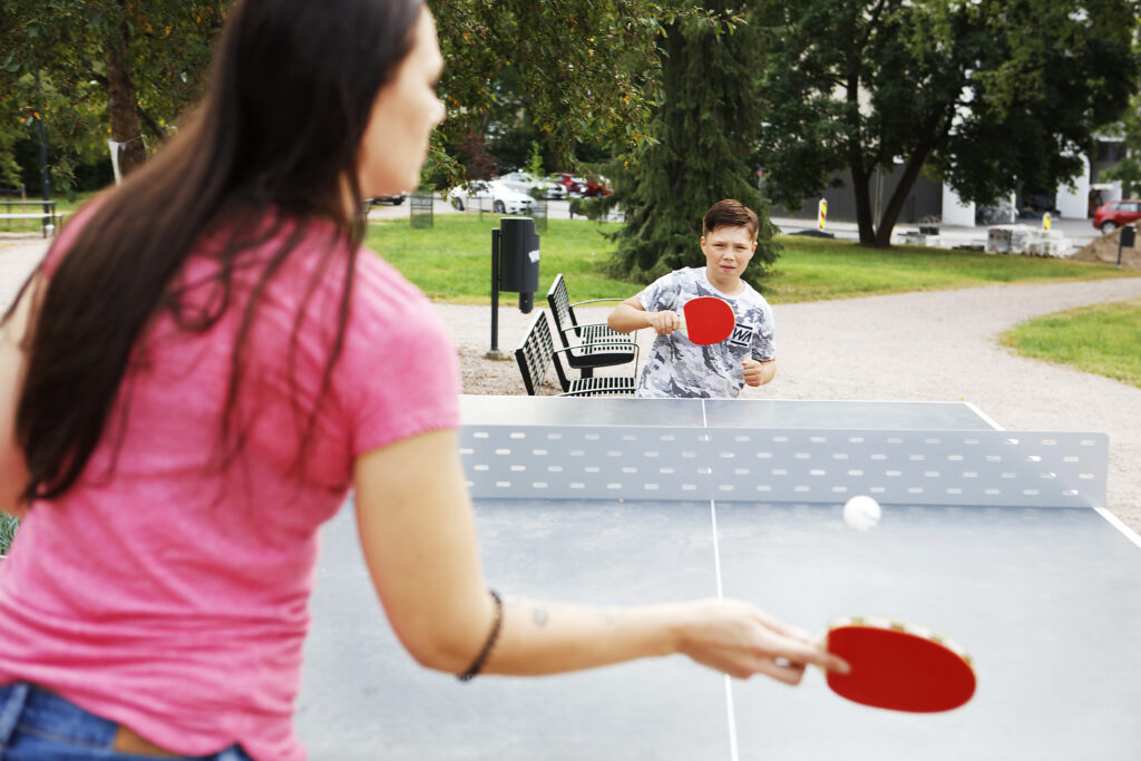Nainen ja poika pelaavat pingistä ulkona. On kesä.