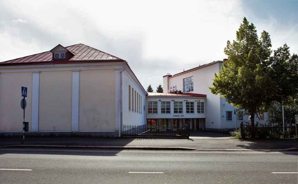 Kesäinen kuva Riihimäen lukion rakennuksesta kadulta päin kuvattuna.