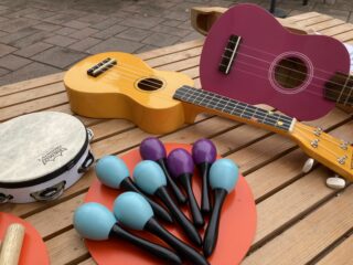 Lasten soittimia, kaksi pientä kitaraa, tamburiini ja marakasseja puisella pöydällä ulkona.