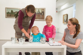 kaksi lasta ja kaksi aikuista tutkimassa museon näyttelyn esineitä.