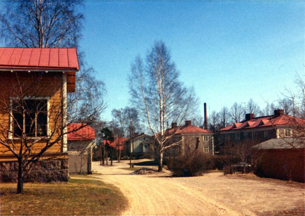 Vanhanaikainen värikuva Rautienpuistossa. Kuvassa hiekkatie ja vahoja taloja.