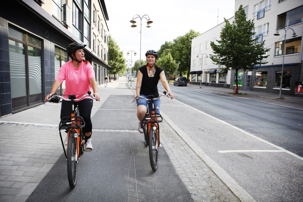 Kaksi naista pyöräilee kaupunkipyörillä kesällä Riihimäen keskustassa.