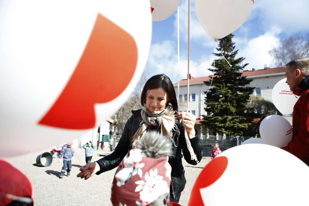 A woman holds a balloon and gives one of them to a child in front of her.