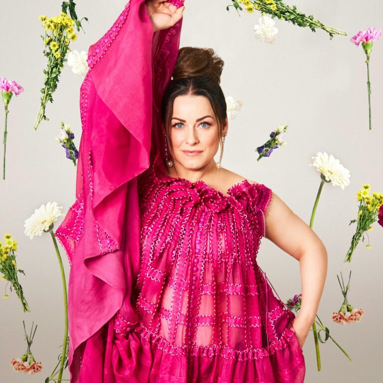 Kuvassa laulaja Erin punaisessa mekossa. Kuvan taustalla kukkia.