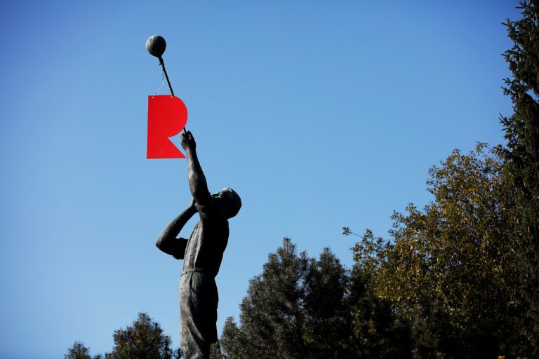 A statue of a glassblower with a hanging red letter R.