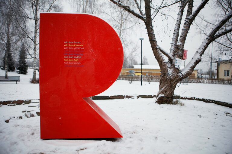 Suuri punainen R-patsas Jukka Jalosen puistossa. On talvi, maassa on lunta.