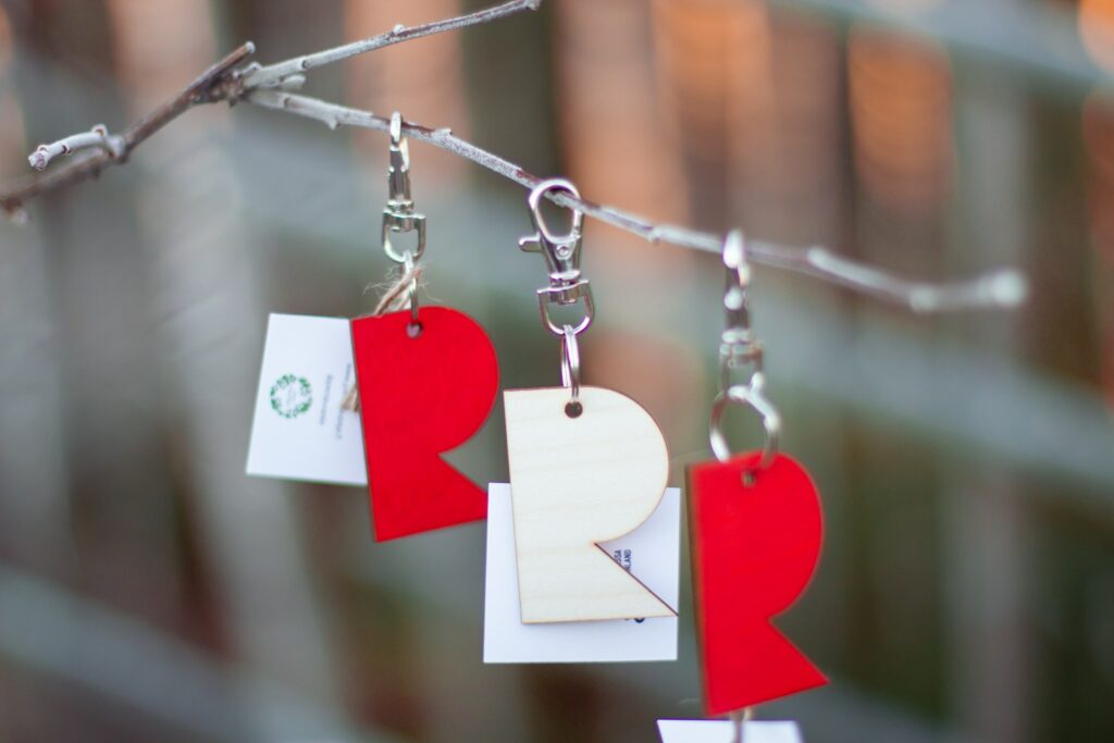 Two red and one white key chain hanging on a tree branch.