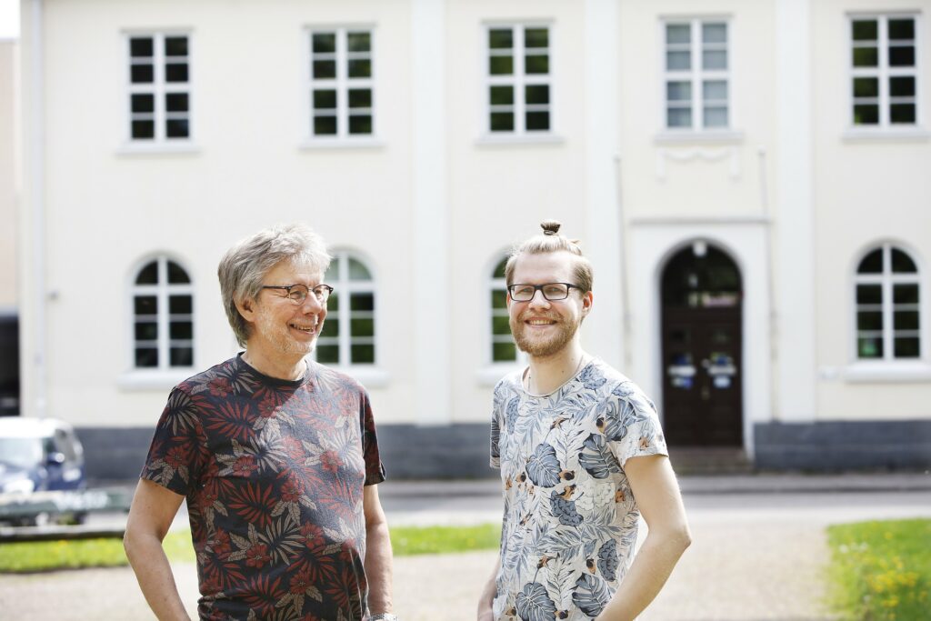 Arto and Joer Pöllänen are standing next to each other and smiling. In the background, a white civic college building.