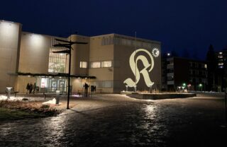 En kvällsbild av biblioteket i Riihimäki, med den dekorativa bokstaven K reflekterad på väggen