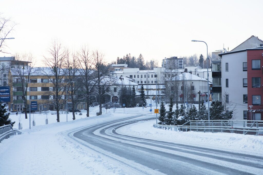 Talvinen katunäkymä. kadun varrella kerrostaloja ja puita.