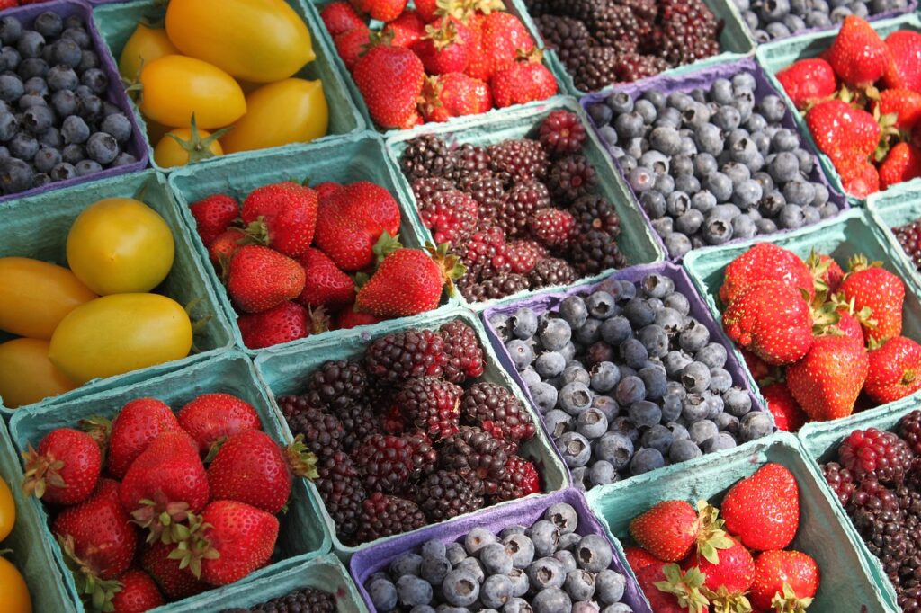 Boxes of yellow tomatoes, strawberries, blackberries and blueberries.