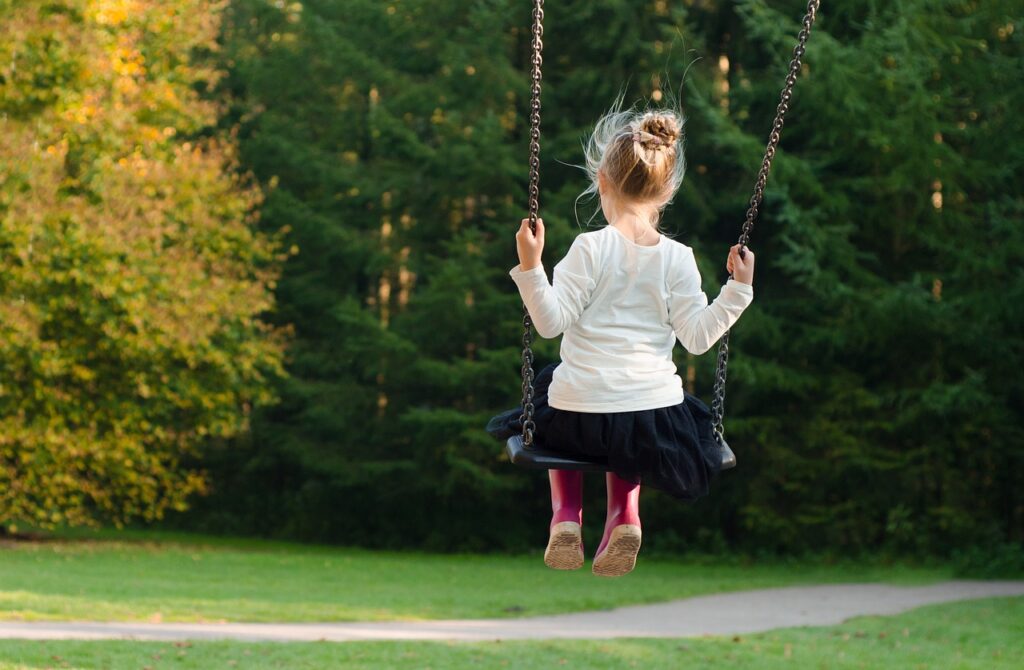 A girl swinging her back to the viewer. Forest in the background.