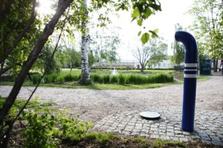 Jukka Jalosen puistossa oleva ääniteos, johon kuuluu maassa oleva laatta ja sinivalkoinen putki. Taustalla näkyy lampi ja suihkulähde.