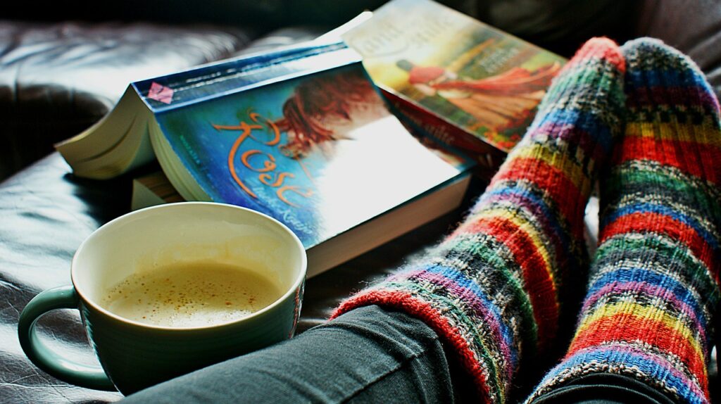 Jalat joissa värikkäät villasukat. Vieressä kaksi kirjaa ja kahvikuppi.