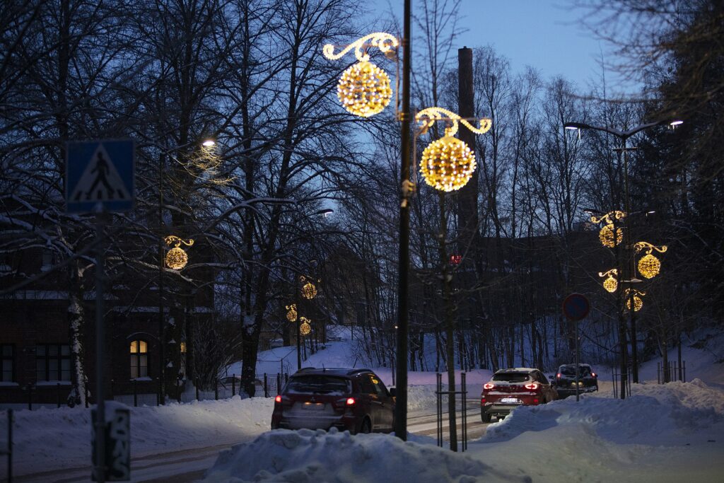 Pallomaisia jouluvaloja kadun varren valopylväissä. Katu on luminen ja siellä ajaa autoja.