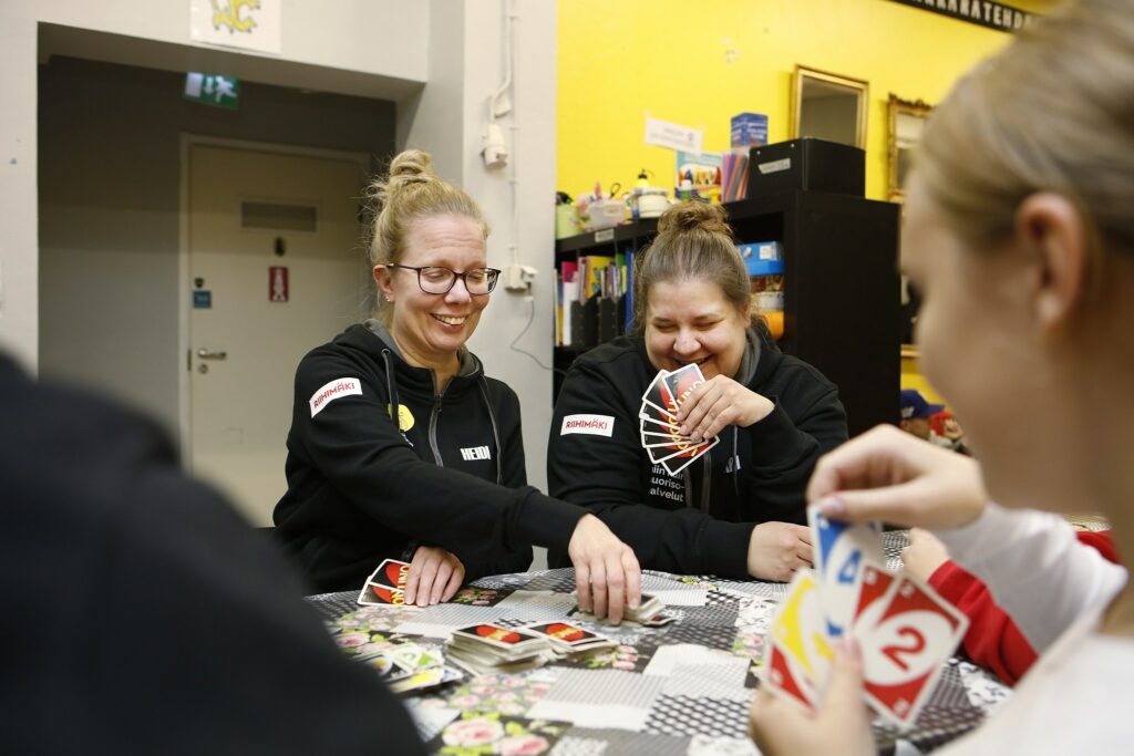 Två kvinnor som spelar kort med ungdomar.