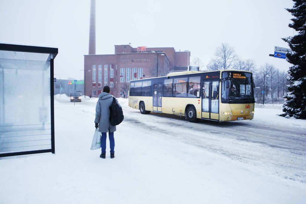 Bussipysäkillä seisoo henkilö ja bussi ajaa ohi.