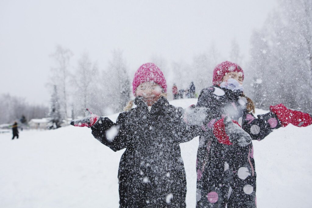 Kuvassa kaksi tyttöä lumisateessa heittelee lunta