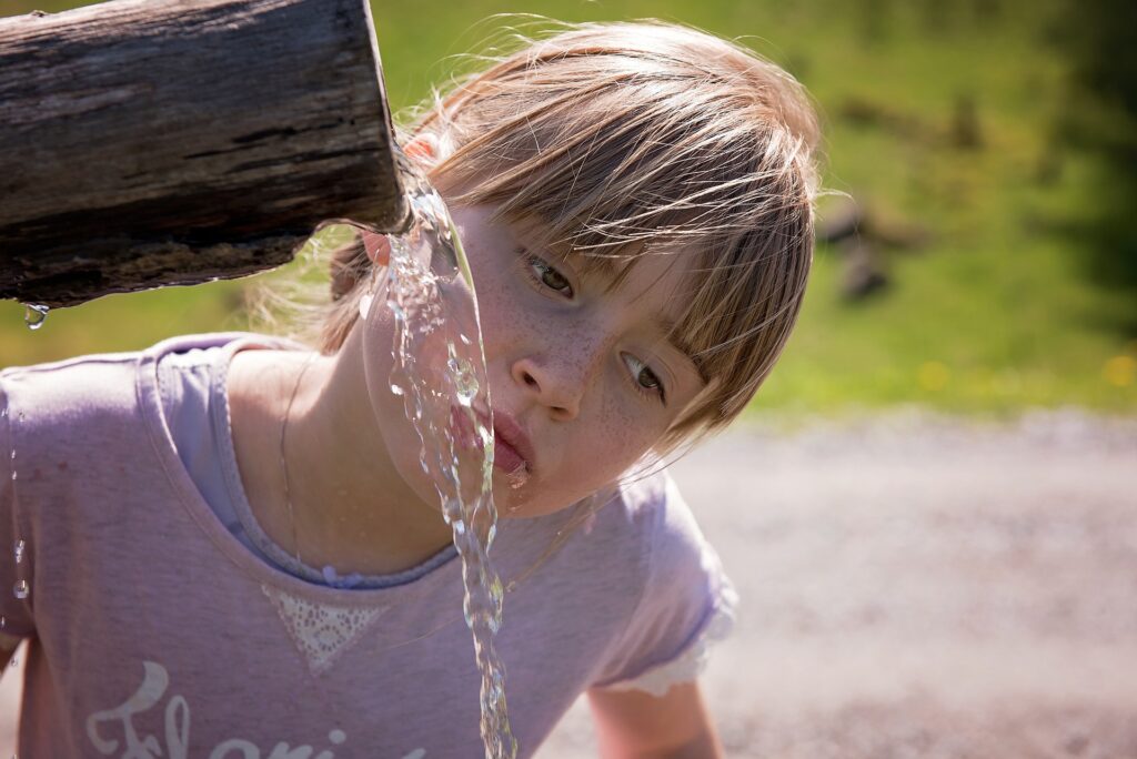 The girl drinks water from the well.