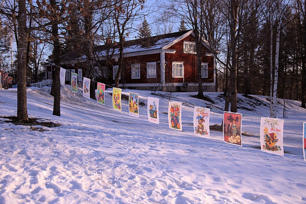 Kaupunginmuseon punainen puutalo lumisessa maisemassa puiden katveessa.