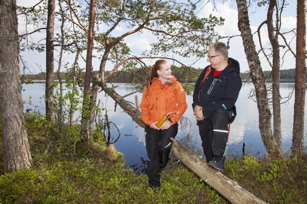 Nainen ja mies juttelemassa järvimaisemassa