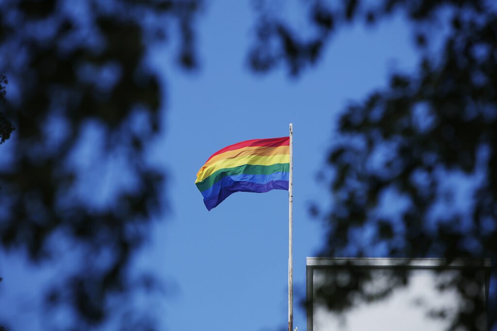 Pride-lippu liehuu sinistä taivasta vasten sateenkaaren väreissä.