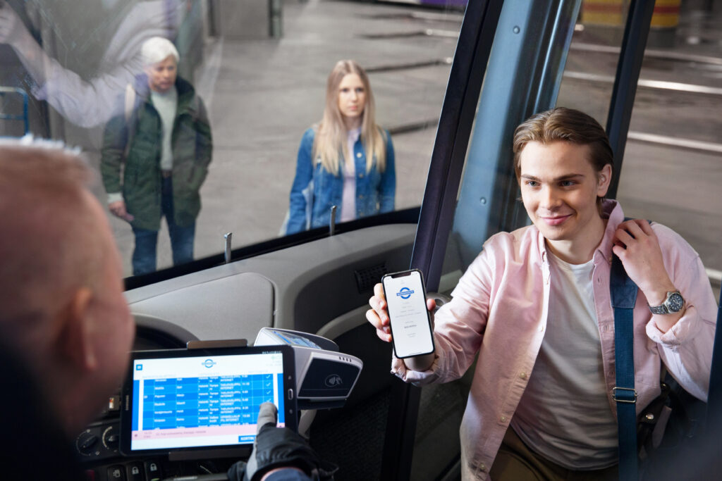 Nuori henkilö nousemassa bussiin ja näyttämässä kuljettajalle kännykästään lippua.