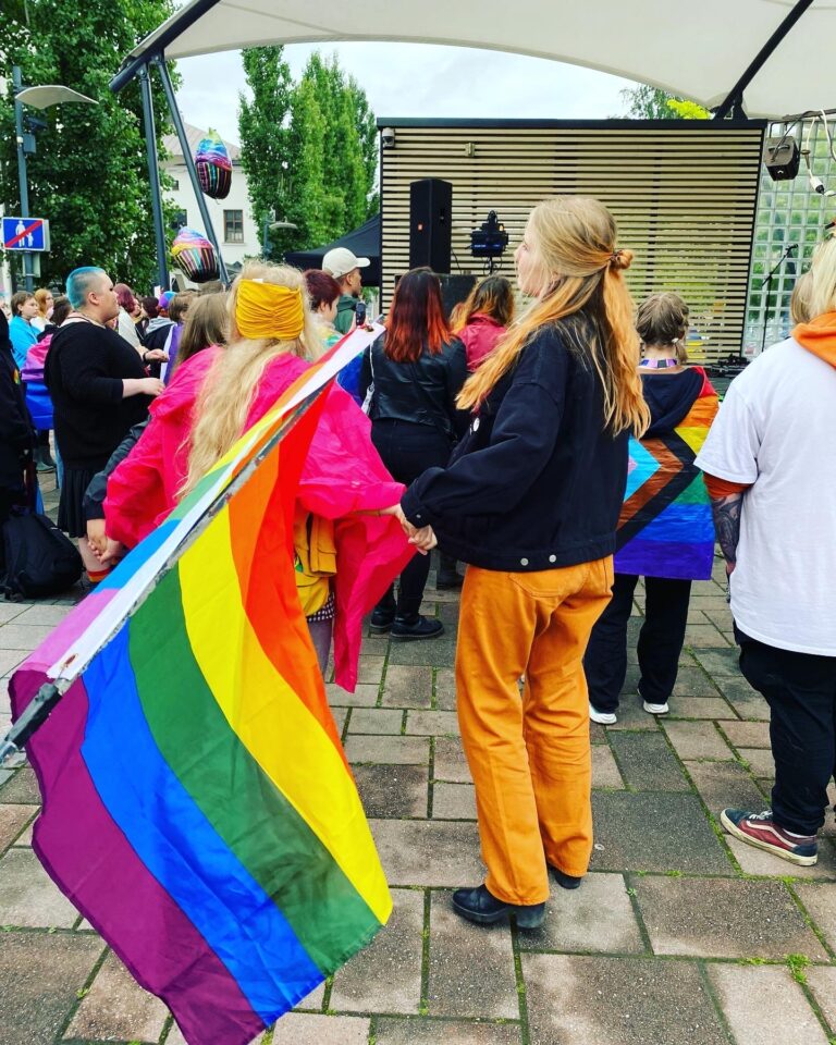 A pride flag is waving in the front and dancing people in the back.