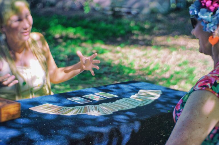 Two women are sitting at a table. Tarot cards have been spread on the table.