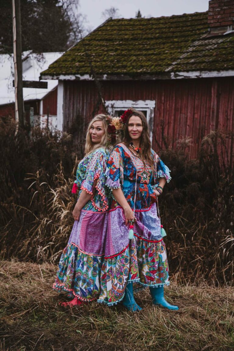 Two women in long dresses stand in a country landscape.