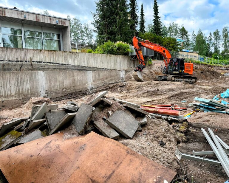 Kuvassa kaivinkone purkaa Riihimäen uimahallin ulkoseinän tukimuuria. Kuvan edustalla myös muuta purkujätettä.