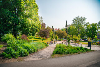 Kesäisen vehreä lounaspuisto on hyvä oleskelupaikka. Kuvassa näkyy puiston useat pöydät ja upeat kasviistutukset.
