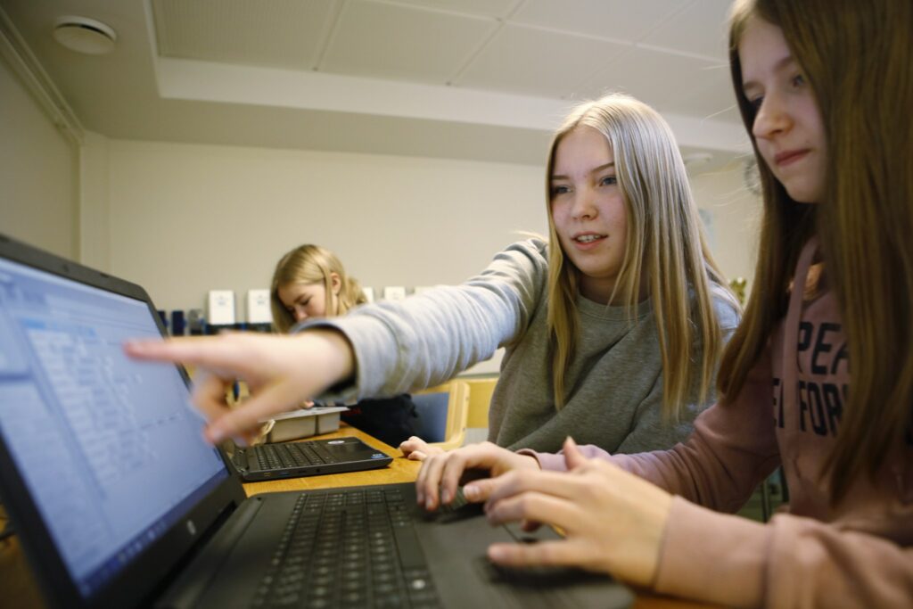 Kaksi nuorta koulussa tietokoneen äärellä, toinen osoittaa kuvaruudulta toiselle jotain.
