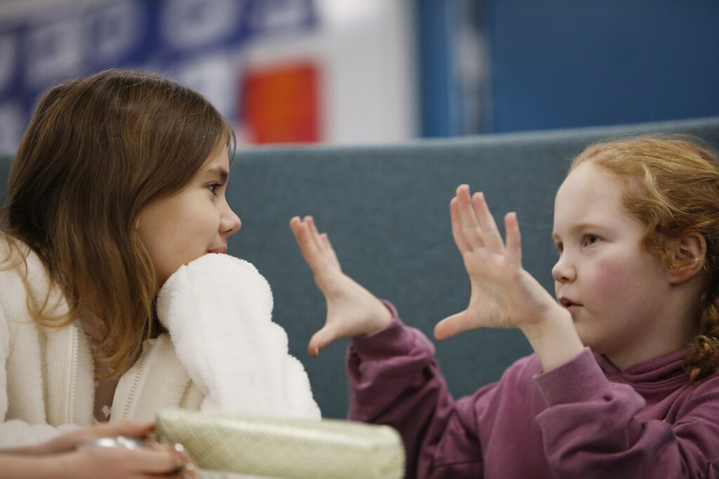 Two students in the school premises talking to each other. One gestures with his hands, the other listens.