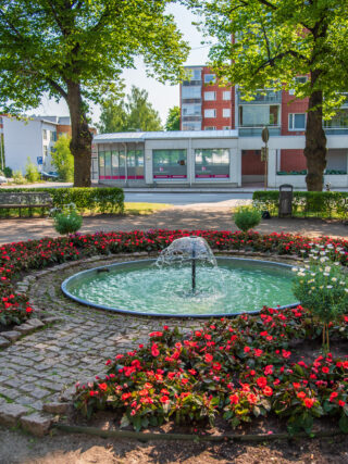 In the middle of the triangle park there is a small water feature with a fountain, spring and summer flowers are planted in the circular planting area.