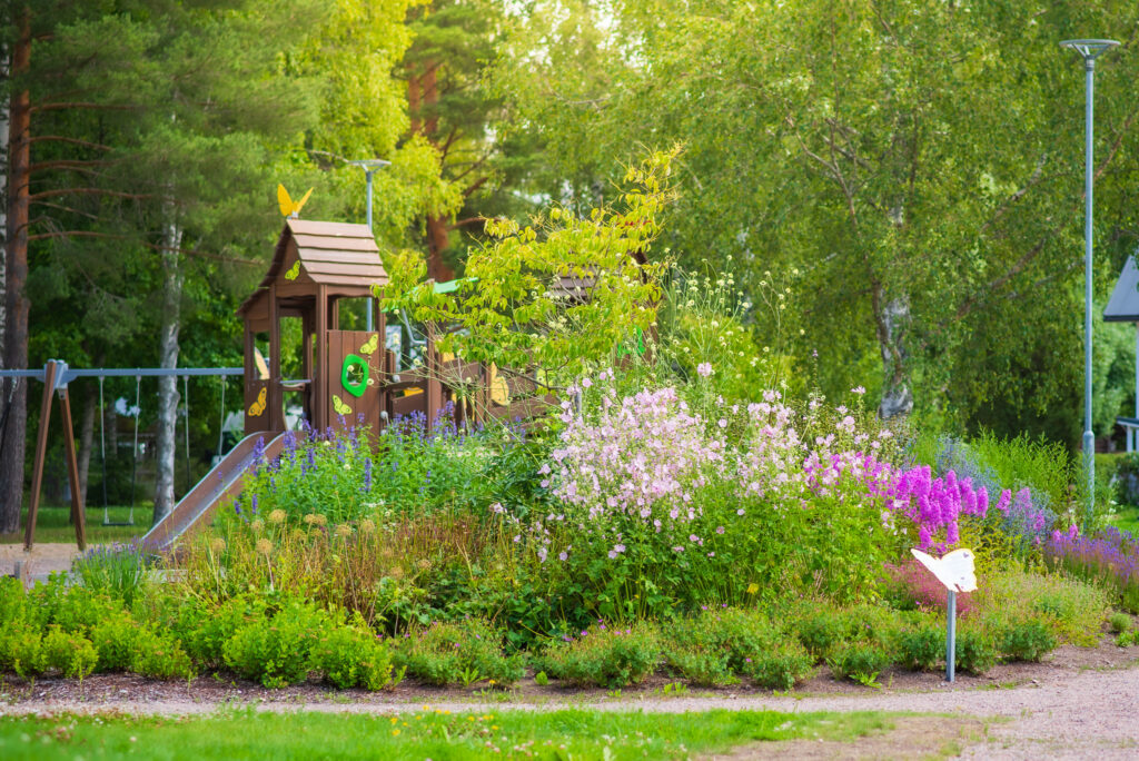 Kesäinen leikkipuisto, jossa vehreät kukkaistutukset.