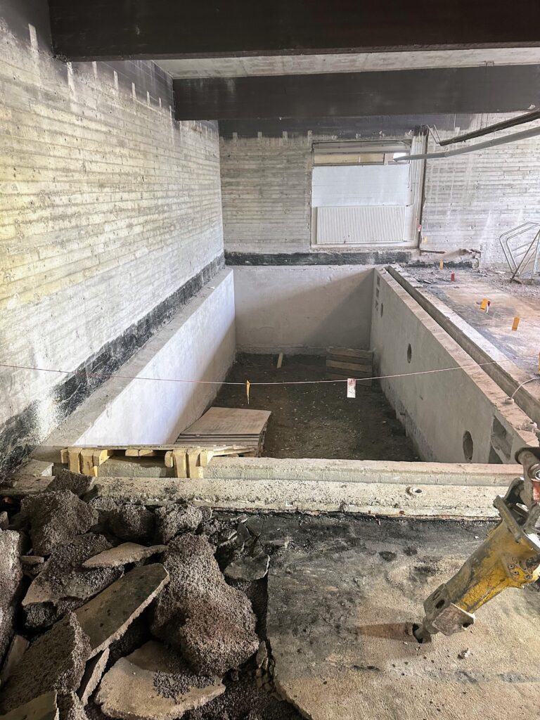 Kuvassa tilaussaunan allas, jonka pohja on purettu pois. Myös vanhat saunojen ja suihkujen seinät ovat myös pois. Kuvattu 25.9.2023.