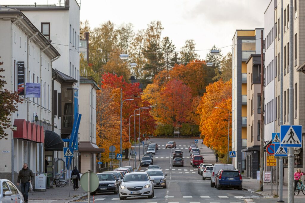 Ylöspäin nousevalla keskustan kadulla autoja, puut ruskan väreissä taustalla.