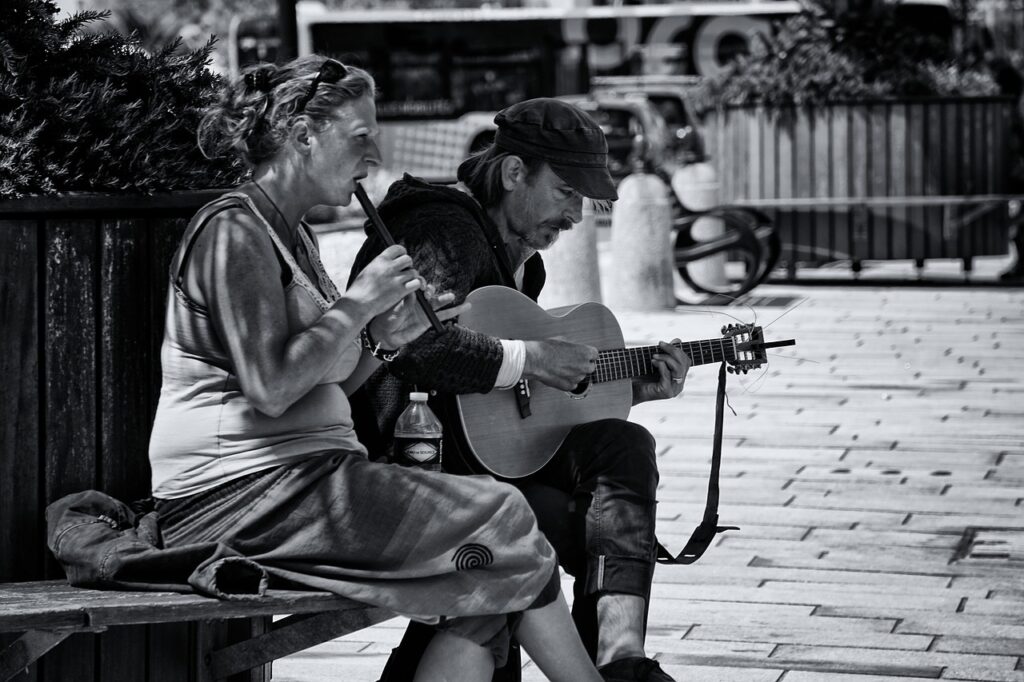 On a park bench, a man plays the guitar and a woman plays the flute.