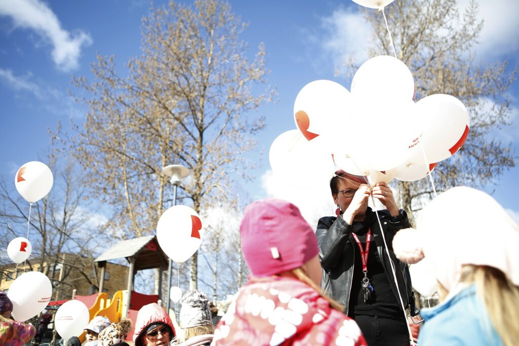 A woman distributes balloons with the Riihimäki logo to children in a playground.