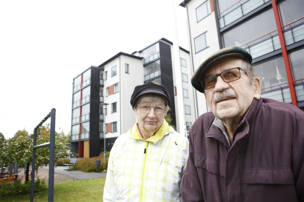 Seija ja Matti Hellström yhdessä ulkona valkoinen uusi kerrostalo taustallaan.