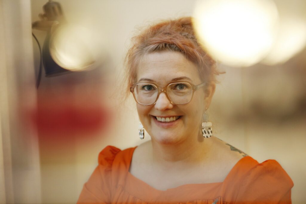 Veera Kannosto happily looks at the camera wearing an orange dress.