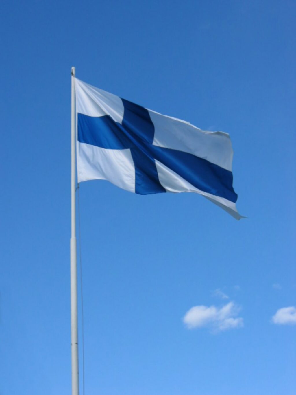 Suomen lippu liehumassa lipputangossa ja sinistä taivasta.