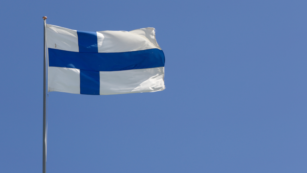 Finland's blue cross flag flutters against the blue sky.