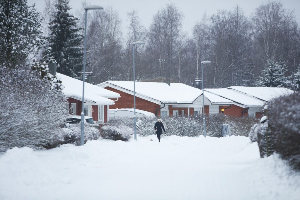 Luminen tie, jonka varrella punatiilisiä pientaloja ja koiranulkoiluttaja kävelemässä niiden edustalla.