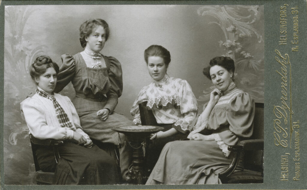 Vanhanaikainen mustavalkoinen valokuva neljästä naisesta, jotka ovat ystävyksiä.