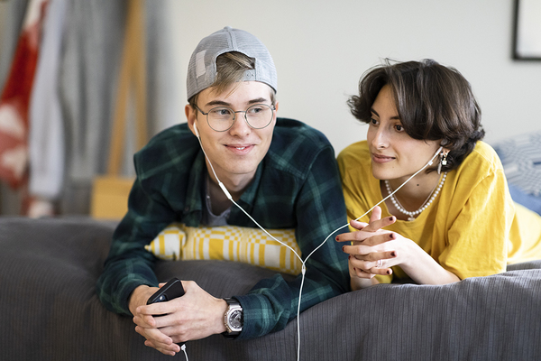 A young man and woman are listening to an audio book together and lying on the bed.