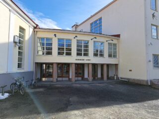 Valkea kaksikerroksinen kivirakennus ovineen, seinässä lukee Riihimäen lukio.
