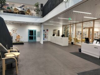 Kaksikerroksisen rakennuksen aula, jossa kaksi vastaanottotiski ja penkkejä.